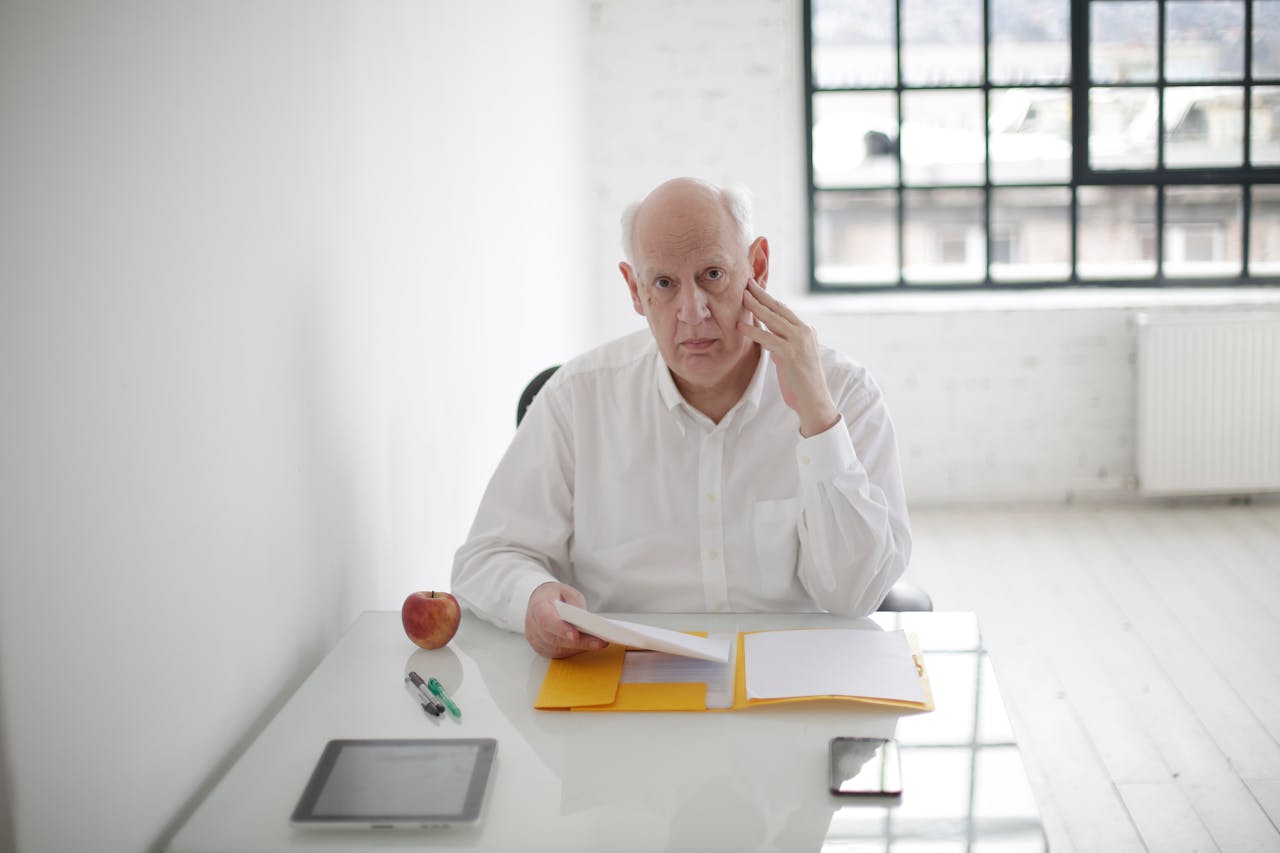 gallery-05 Elderly businessman thinking at desk with documents in modern office.